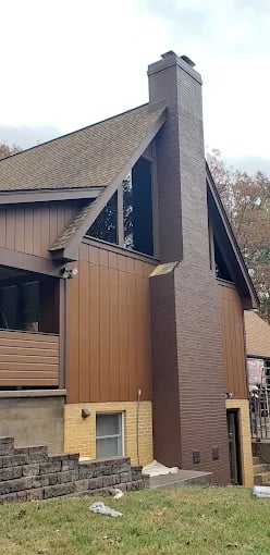 Brown and yellow two-story house with steep roof and chimney