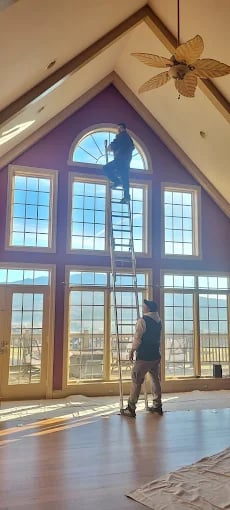 Person on ladder cleaning large arched windows in sunlit room
