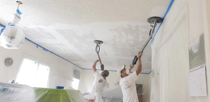 Two painters sanding and smoothing a ceiling with long-handled tools