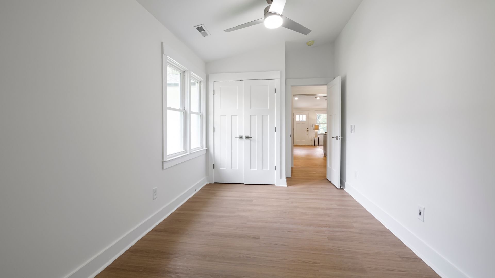 Empty white room with wooden floors, doors, and ceiling fan
