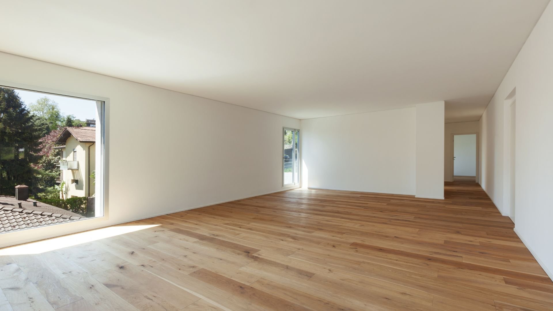 Empty room with wooden floors, white walls, and large windows