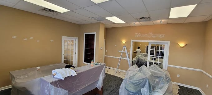 Interior room under renovation with painter on ladder and furniture covered in plastic