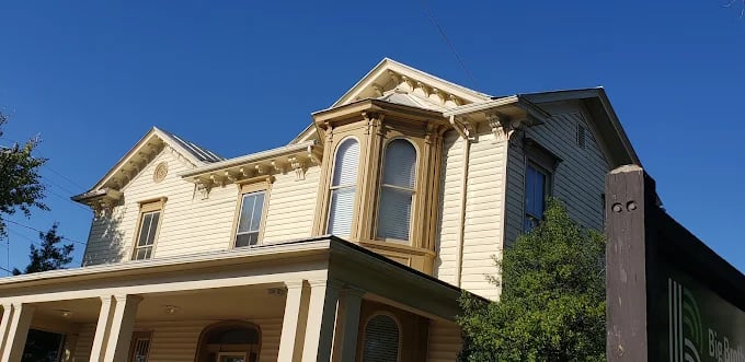 Historic two-story Victorian house with pale yellow siding against blue sky