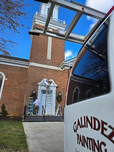 Painters on ladder working on white architectural detail of brick building