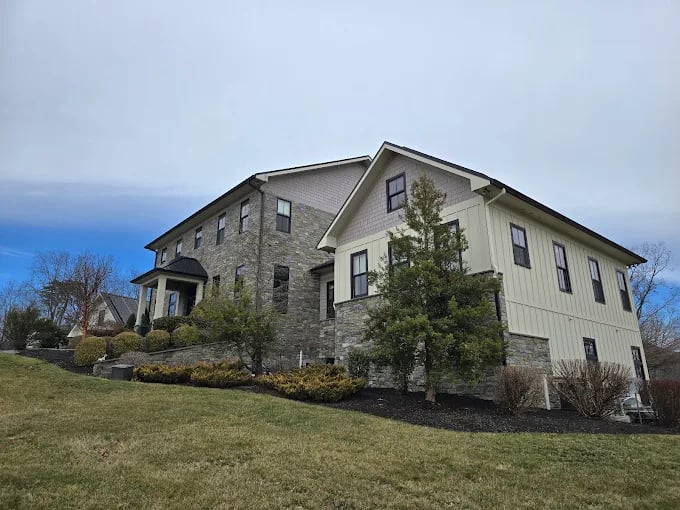 Large two-story stone and white house with trees on grassy hill